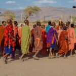 Home Vibrant Maasai group in traditional attire with scenic Tanzanian backdrop.